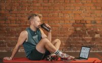 Athletic man sitting on exercise mat with water bottle, taking a break from workout, in a rustic indoor setting.
